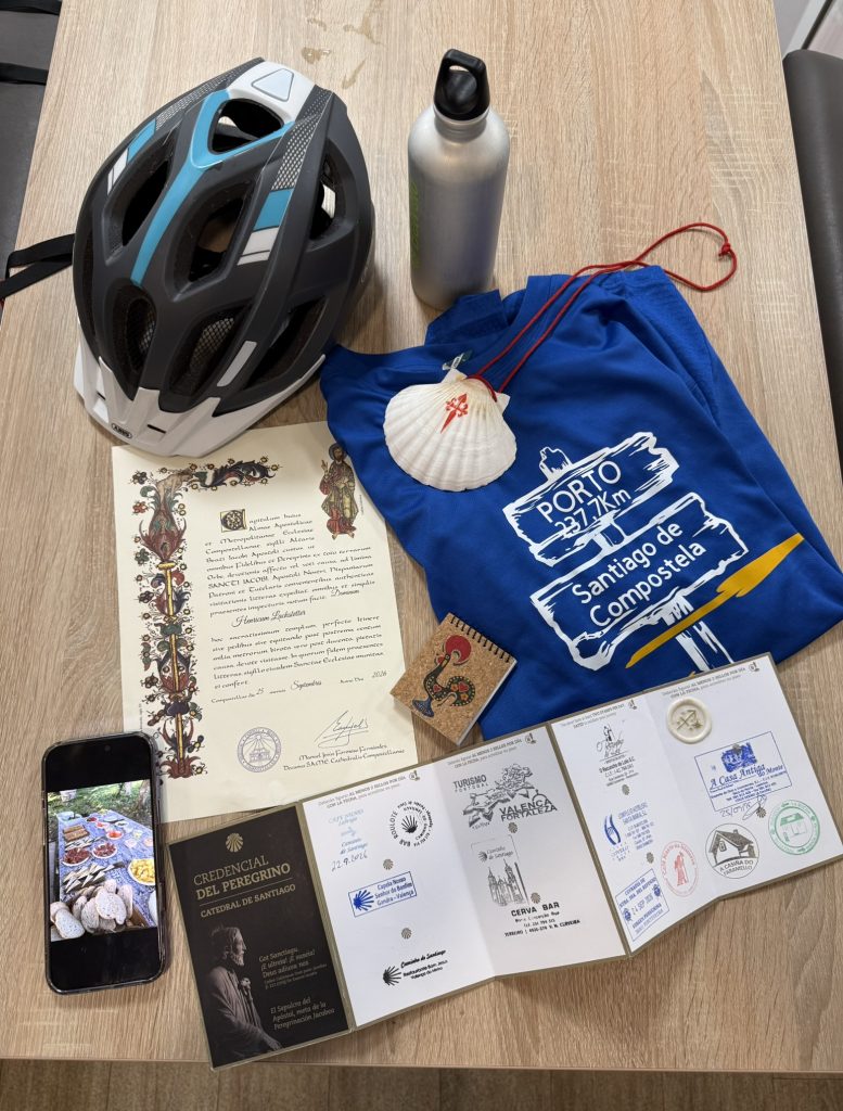 Fahrradhelm, Jakobsmuschel, Compostela und gestempelter Pilgerpass nach der Radtour von Porto nach Santiago.