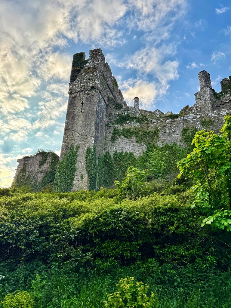 Von unten fotografierte Burgruine mit hohen, efeubewachsenen Steinmauern vor blauem Himmel.