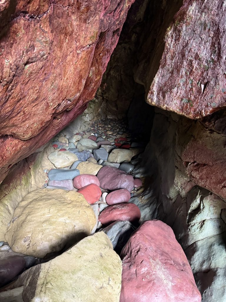 Im Inneren einer engen Felshöhle bei Caerfai Bay liegen runde, bunte Kieselsteine.