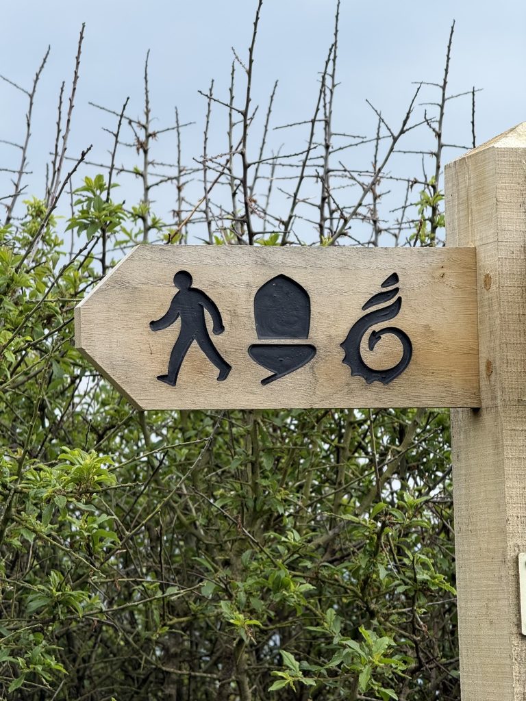 Ein Holzschild mit Symbolen weist an einem Weg bei Caerfai Bay auf einen Wanderweg hin.