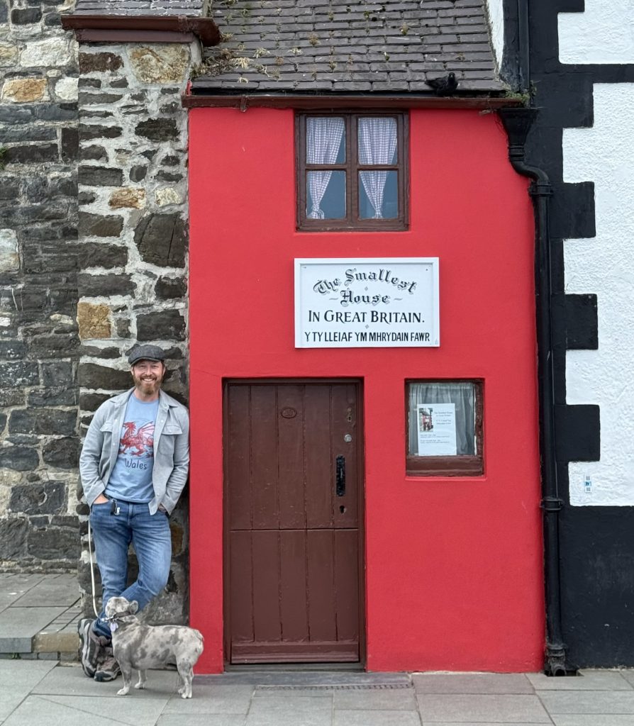 Heiko und Mila stehen neben dem schmalen roten Haus in Conwy, das sich als kleinstes Haus Großbritanniens bezeichnet.