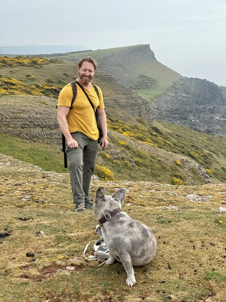 Heiko steht mit Mila auf einem felsigen Küstenpfad oberhalb der Rhossili bay; hinter ihnen erheben sich Steilklippen