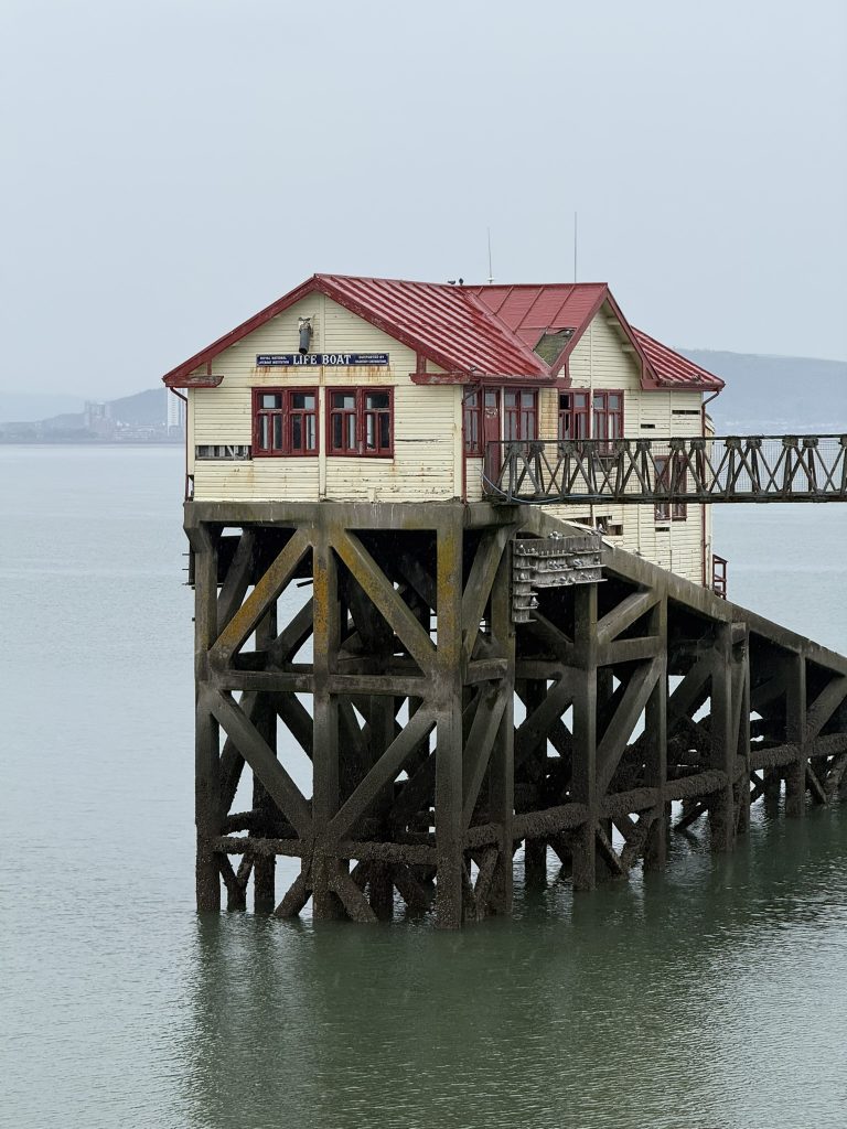 Ein kleines Gebäude auf Stelzen steht am Mumbles Pier über dem Wasser.