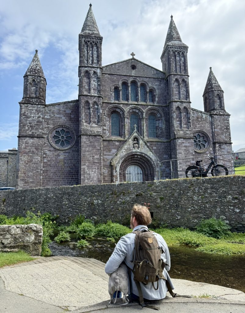 Heiko betrachtet die Fassade der Kathedrale von St Davids von der anderen Seite einer niedrigen Steinmauer.