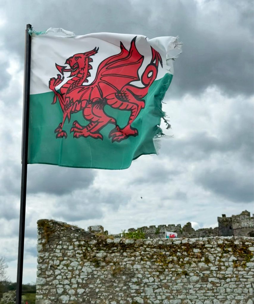 Die walisische Flagge mit rotem Drachen weht über einer steinernen Burgmauer.